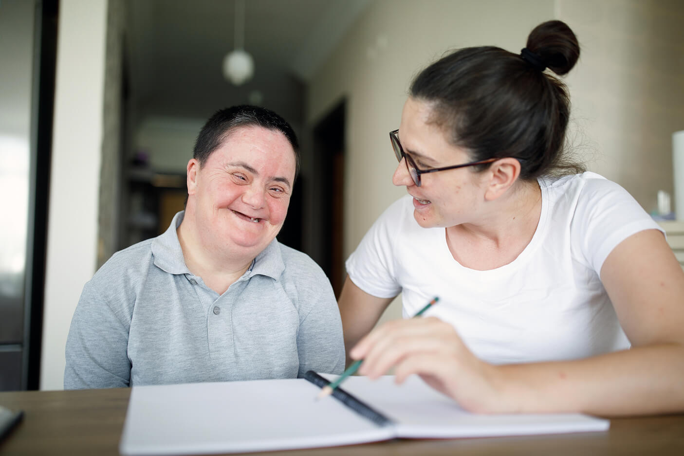 A man with Down syndrome and a support worker laughing over a notebook at a table.