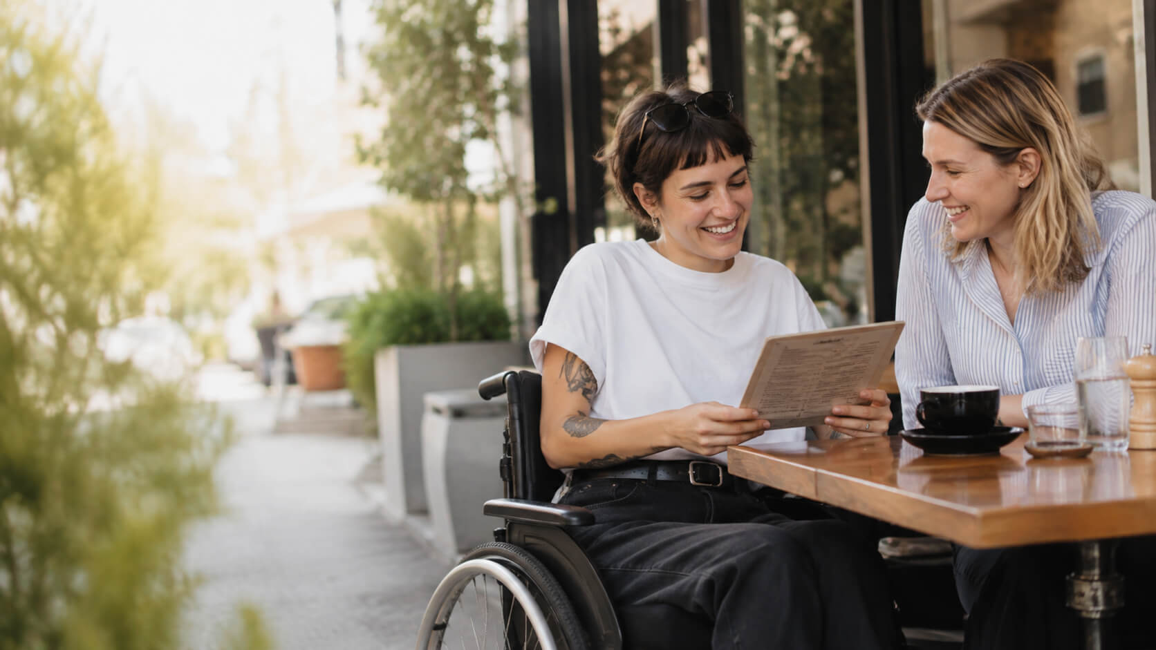 A woman in a wheelchair and a friend reading a menu together at an outdoor café.