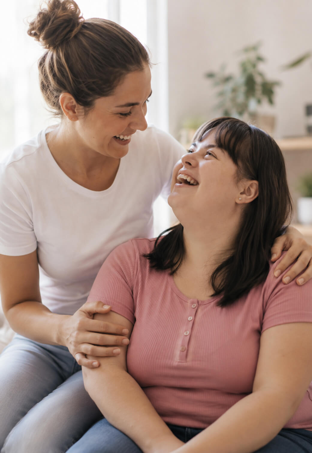 A support worker and a young woman with Down syndrome laughing together at home.