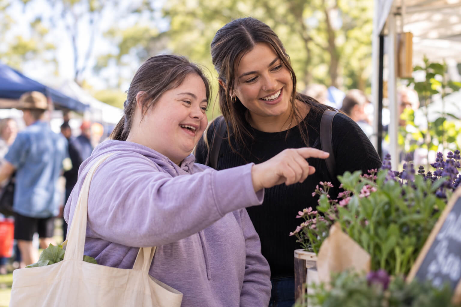 A young woman with Down syndrome and a support worker browsing flowers at an outdoor market.